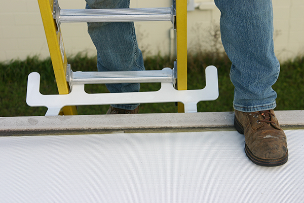 Closeup of man shoe. Man stepping from a yellow ladder on to a white roof. Ladder is secured by a Springfield Ladder Anchor.